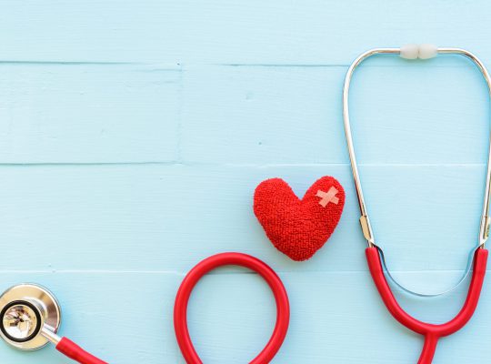 World health day, Healthcare and medical concept. World health day, Healthcare and medical concept. Woman hand holding red heart with Stethoscope, notepad or notebook, thermometer and yellow Pill on Pastel white and blue wooden table background texture.